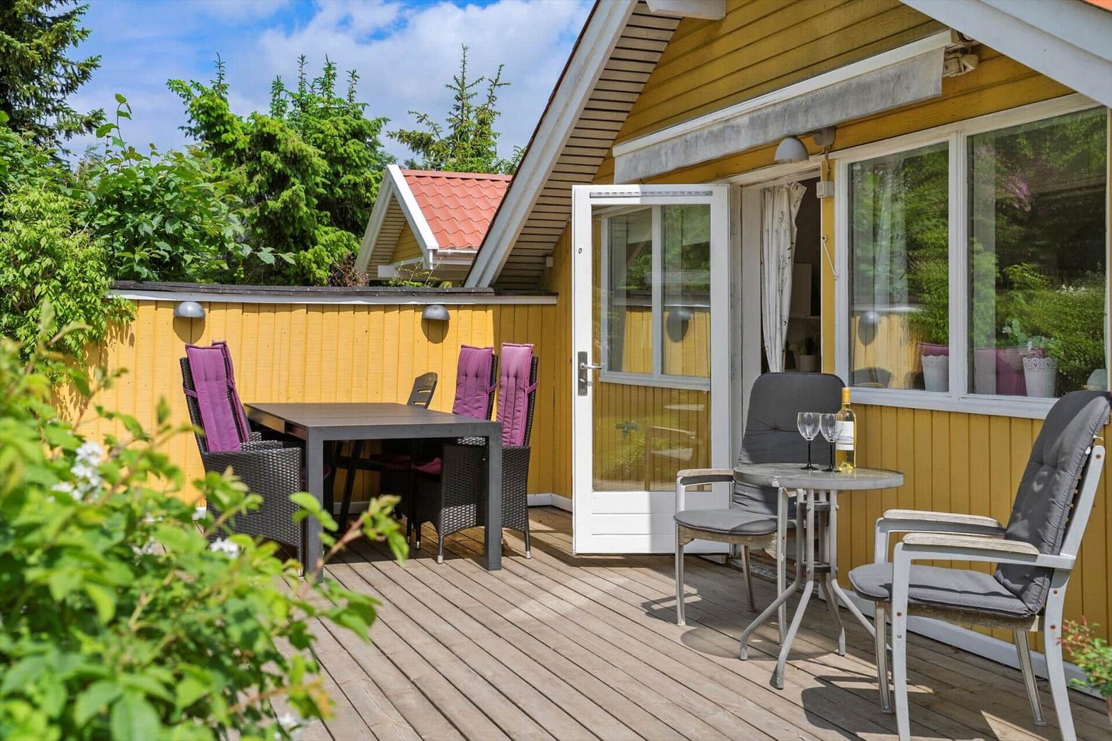 Terrasse mit Tisch, Stühlen und Sitzgelegenheit vor gelbem Haus