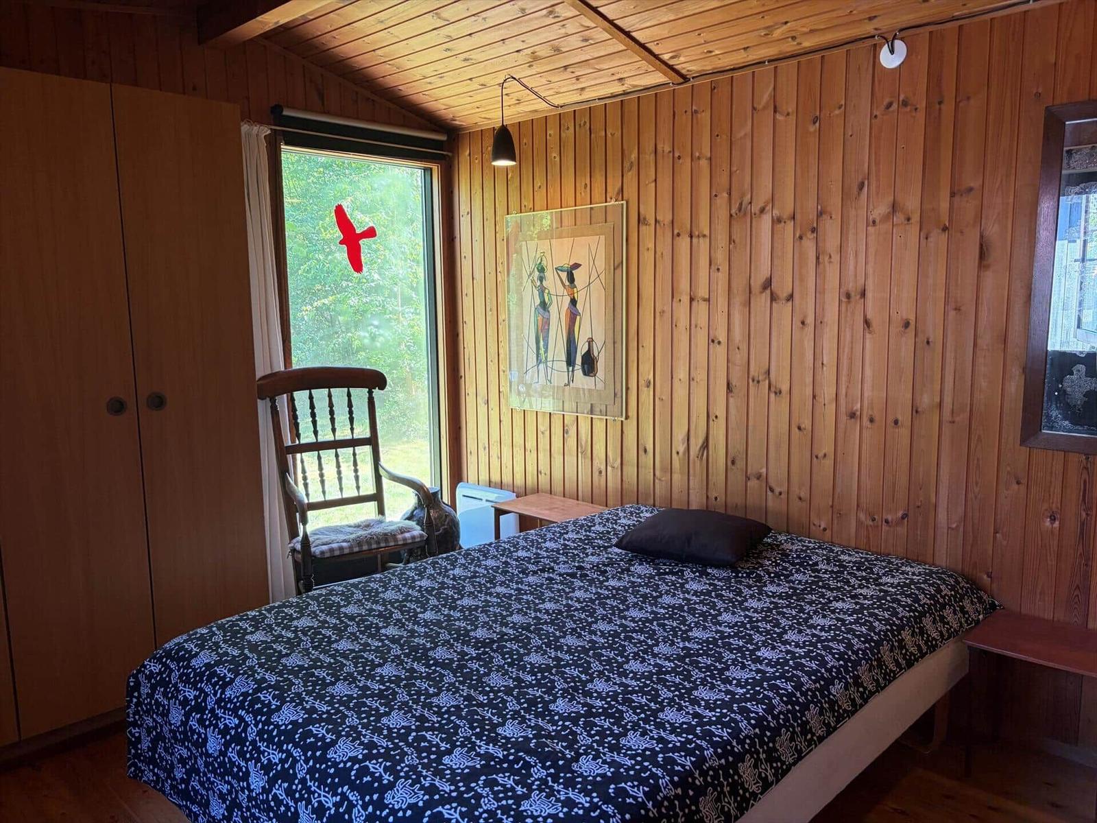 Schlafzimmer mit Holzwand, Bett, Stuhl und Fenster.