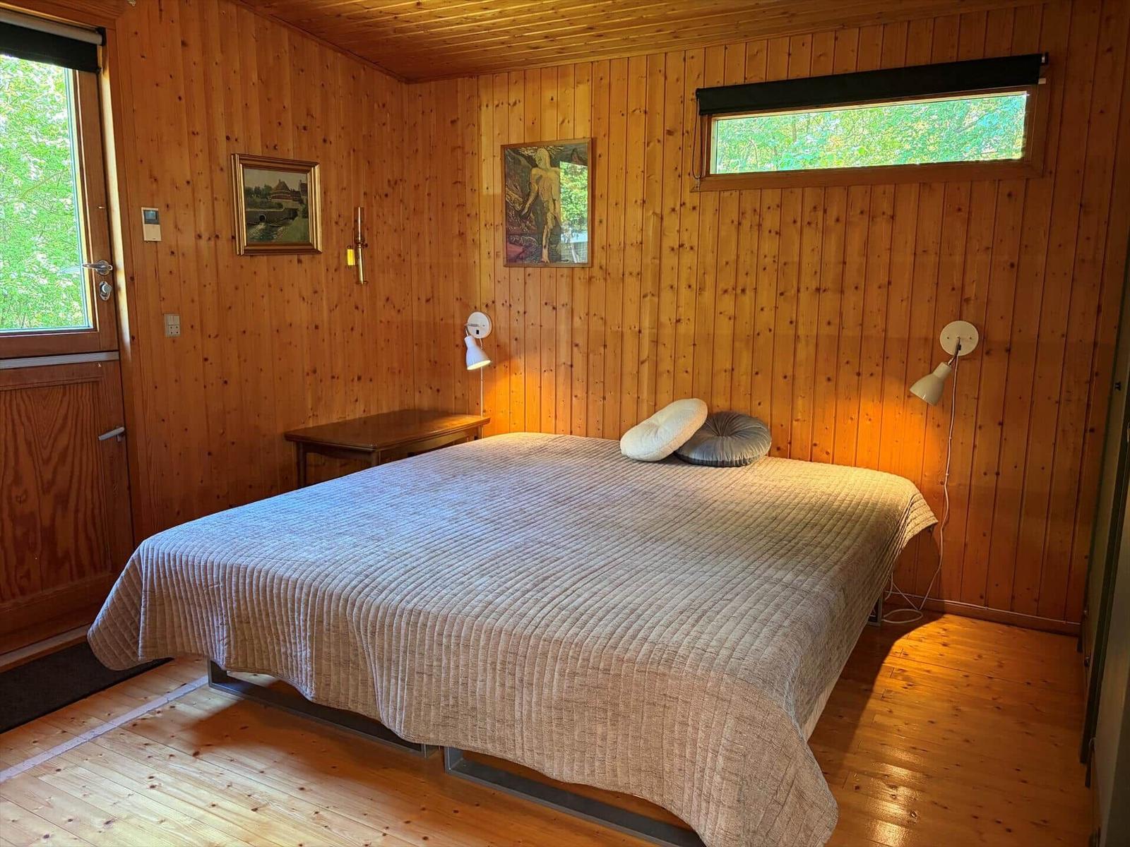 Schlafzimmer mit Holzwand, Bett, Fenster und Wandlampen.