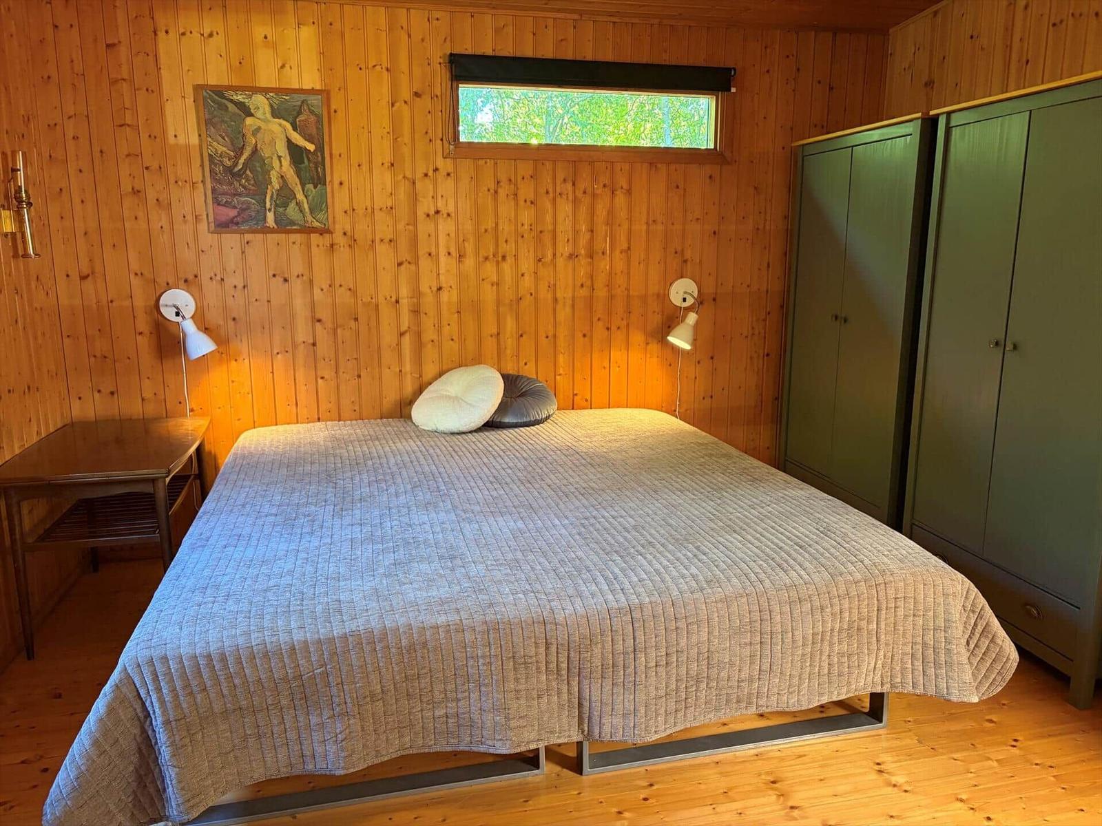 Schlafzimmer mit Holzwand, Bett, Kleiderschränken und Fenster.
