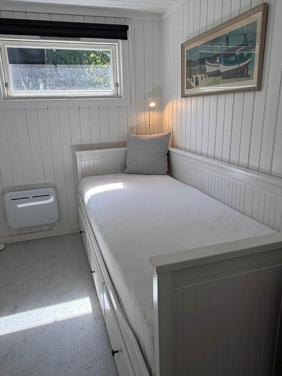 Ein Schlafzimmer mit weißer Matratze, Wandbild und Fenster mit Blick nach draußen.