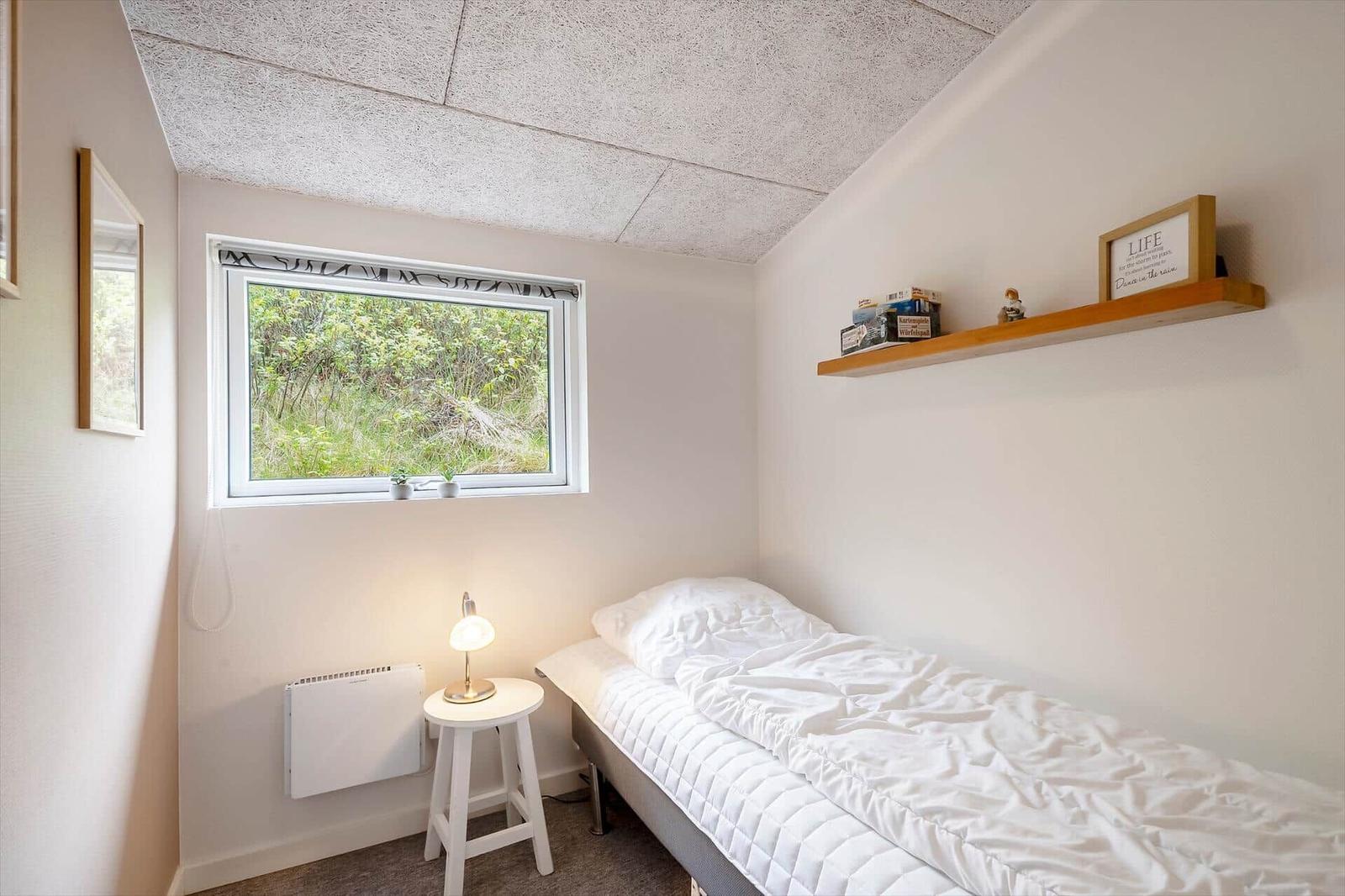 Ein Schlafzimmer mit Einzelbett, Fenster und Holzregal an der Wand.