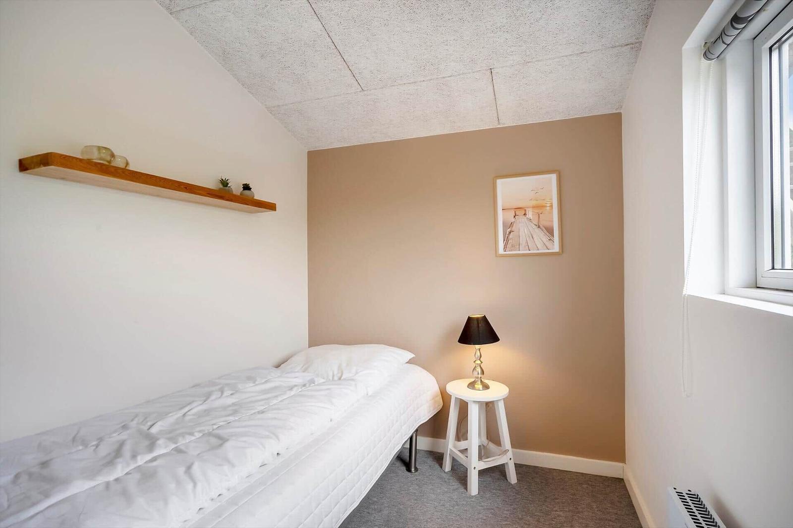 Ein Schlafzimmer mit Bett, Nachttisch und Wandbild. An der Wand hängt ein Bild. Ein Fenster ist sichtbar.