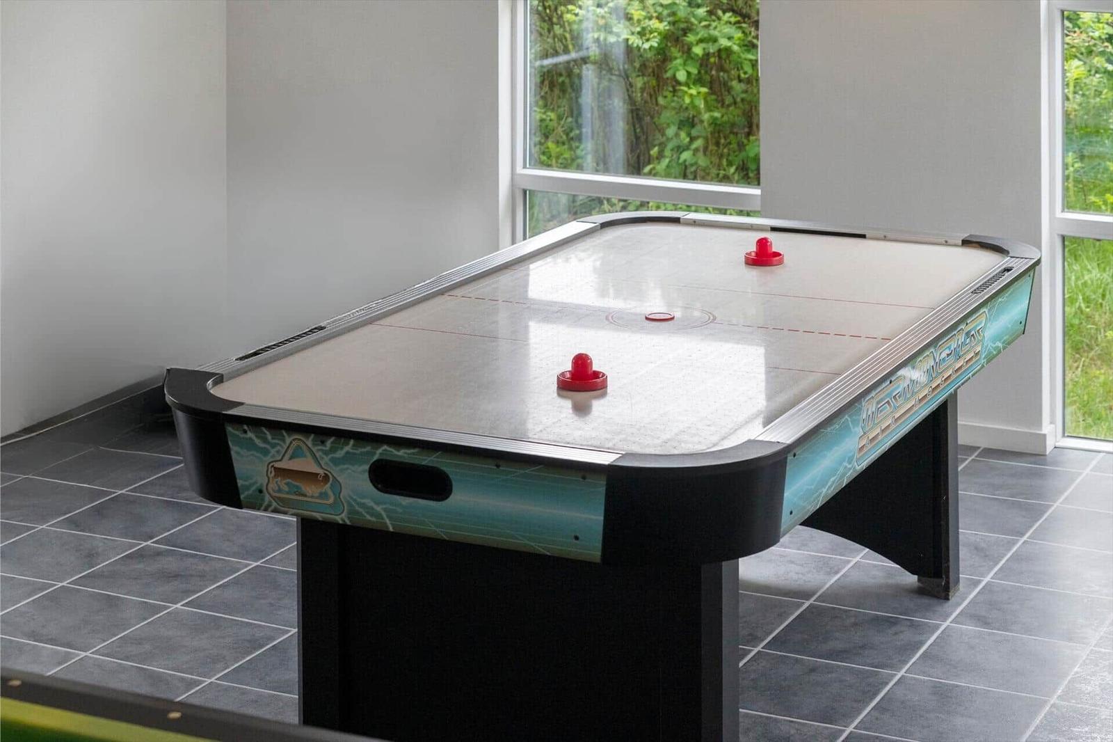 Ein Airhockey-Tisch mit roten Spielsteinen steht in einem Raum mit Fenstern und Fliesenboden.