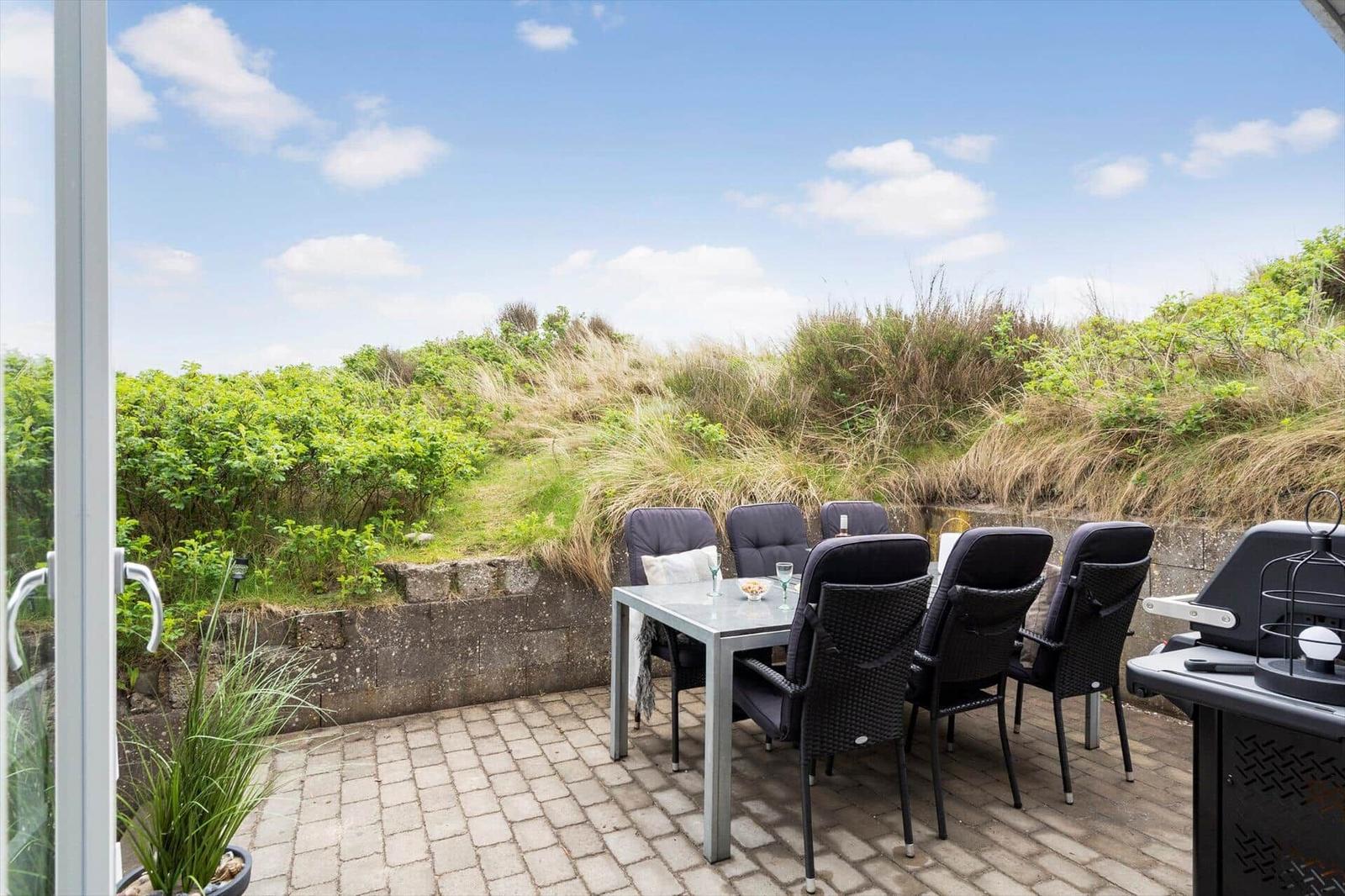 Terrasse mit Tisch und Stühlen, Grill und Blick auf Grünflächen.
