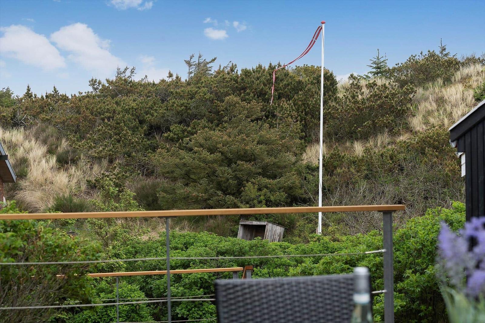 Terrasse mit Blick auf grüne Hänge und einen Mast mit rotem Band.