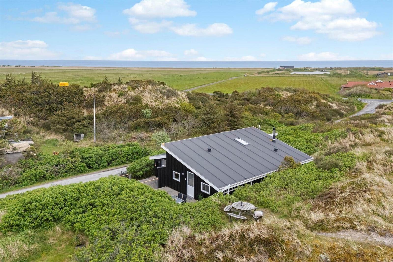 Ein schwarzes Haus mit grauem Dach liegt in einer grünen Landschaft mit Blick aufs Meer.