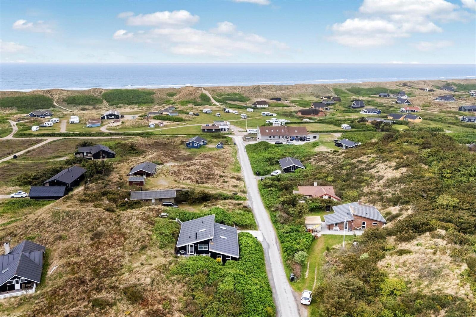 Aerial view of coastal village with houses, dunes, and ocean in background.