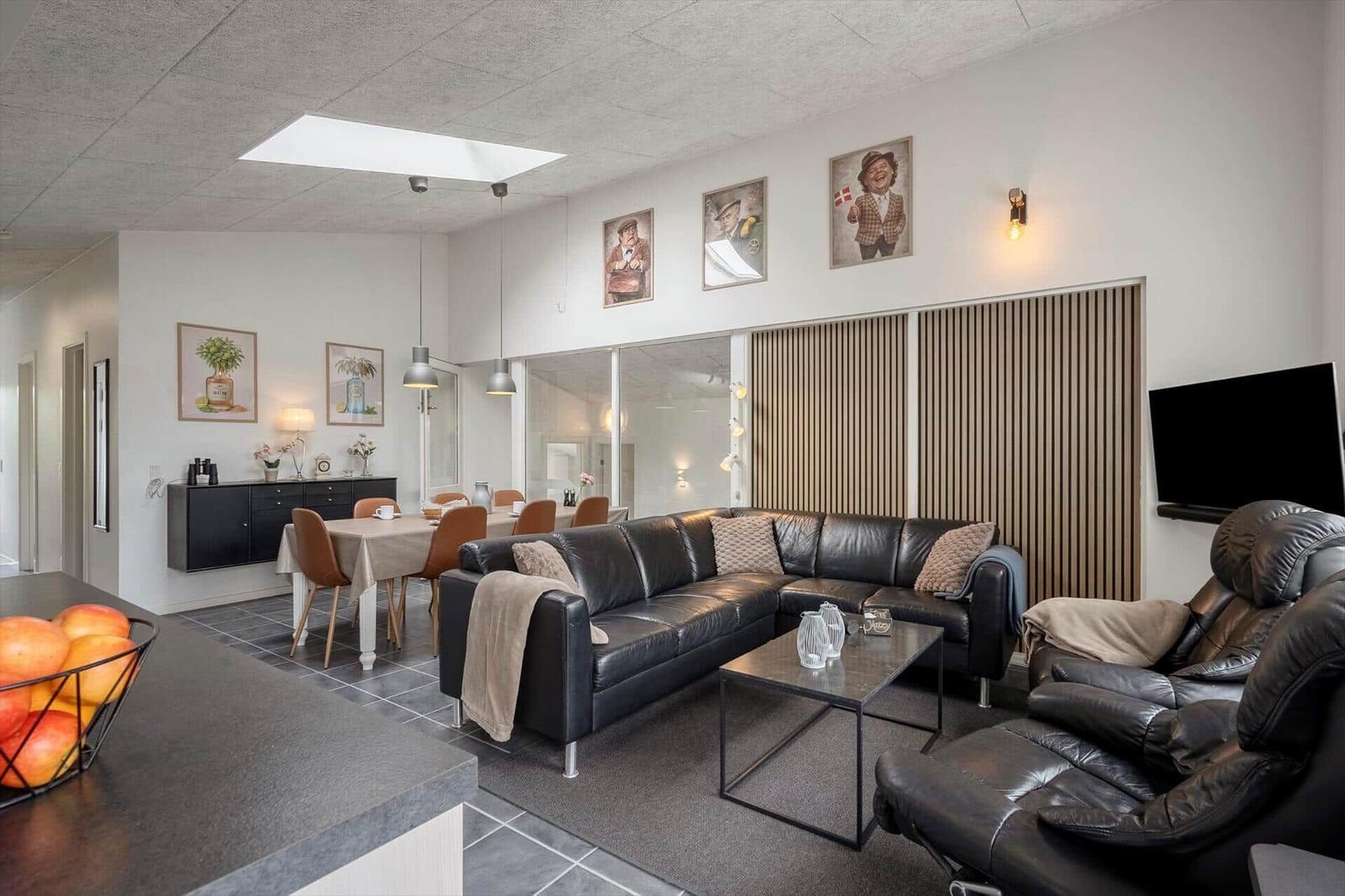 Wohn- und Essbereich mit Ledersofa, Fernseher und Wandbildern.