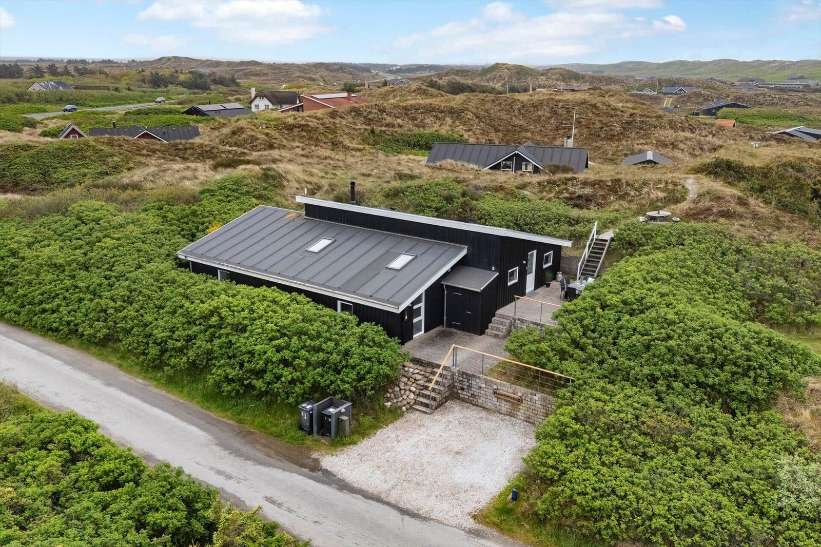 Moderne schwarze Hütte mit Terrasse und Garten in hügeliger Landschaft.