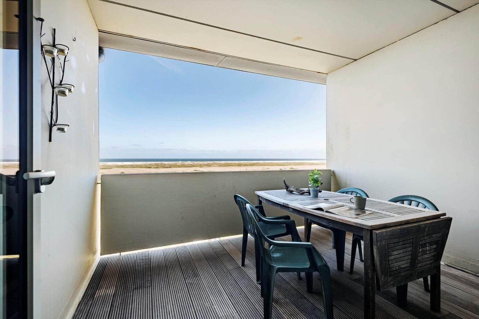 Terrasse mit Tisch und Stühlen, Blick auf Strand und Meer.