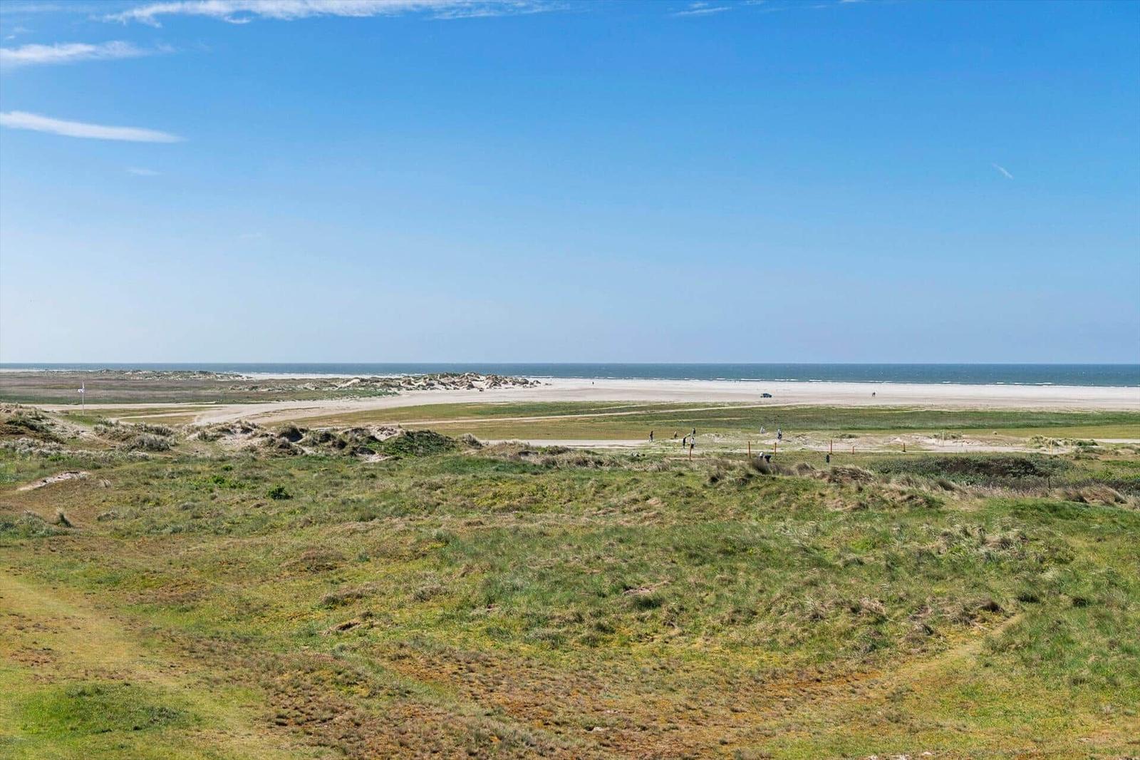 Weitläufiger Strand mit Dünen und klarem Himmel. Menschen genießen die Landschaft.