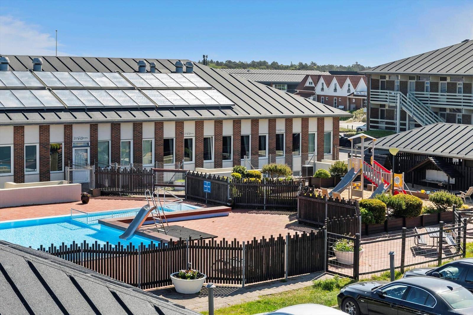 Poolbereich mit Rutsche und Spielplatz vor Wohngebäuden.