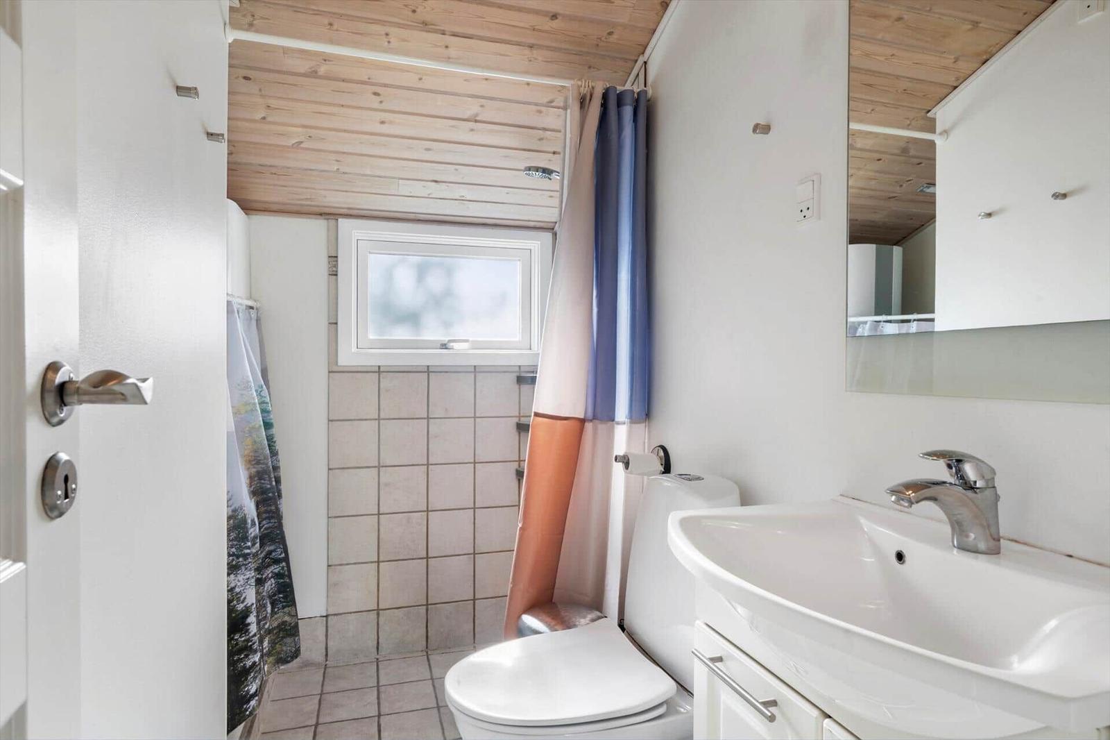 Badezimmer mit Toilette, Waschbecken und Dusche mit Fenster