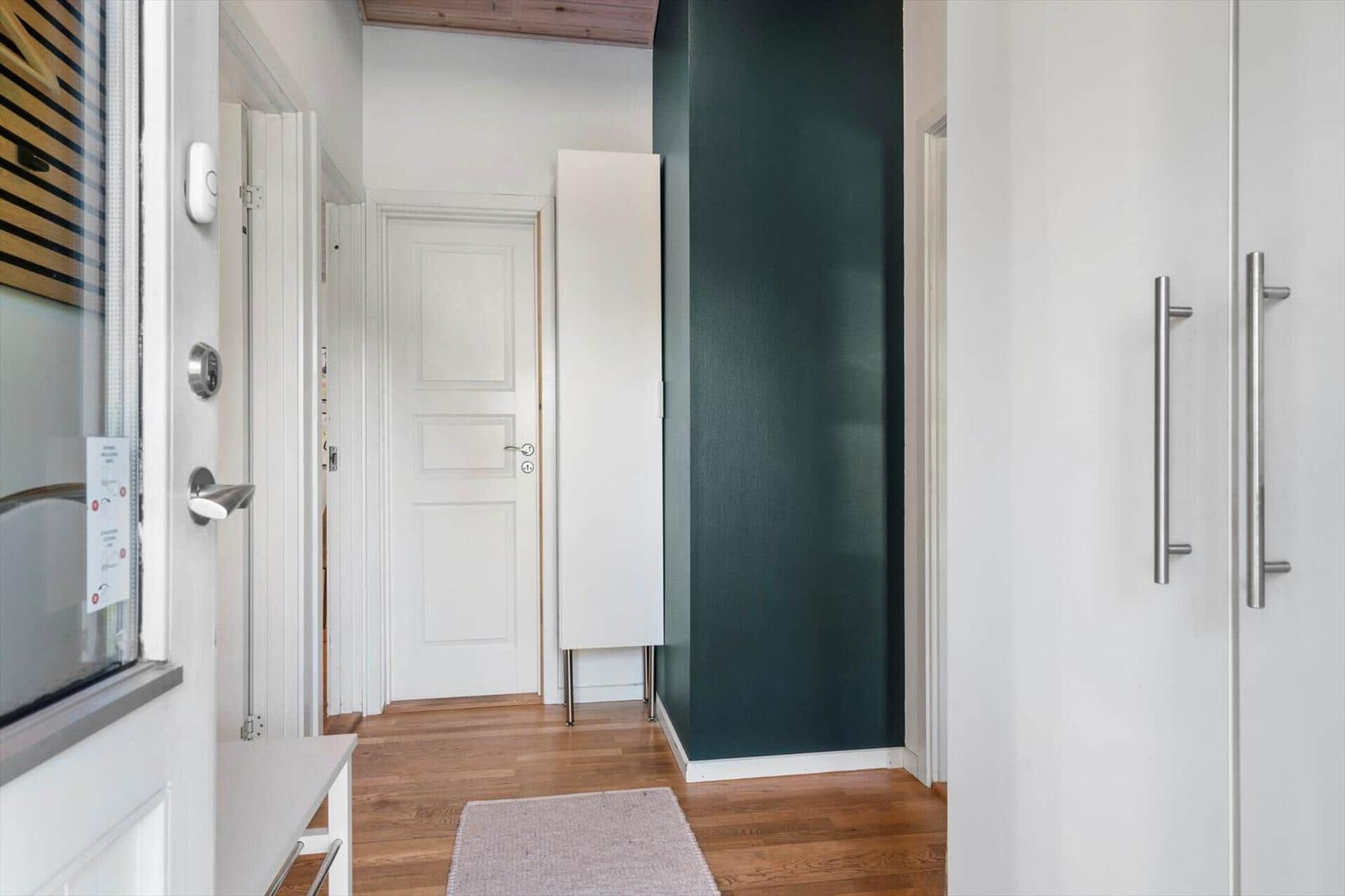 Flur mit Holzboden, weißer Tür und grüner Wand. Kleiner Teppich und Schrank sichtbar.