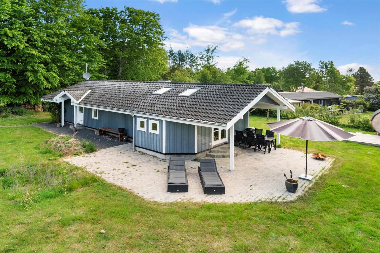 Ein Haus mit Terrasse, Liegestühlen und Grillplatz im Garten.