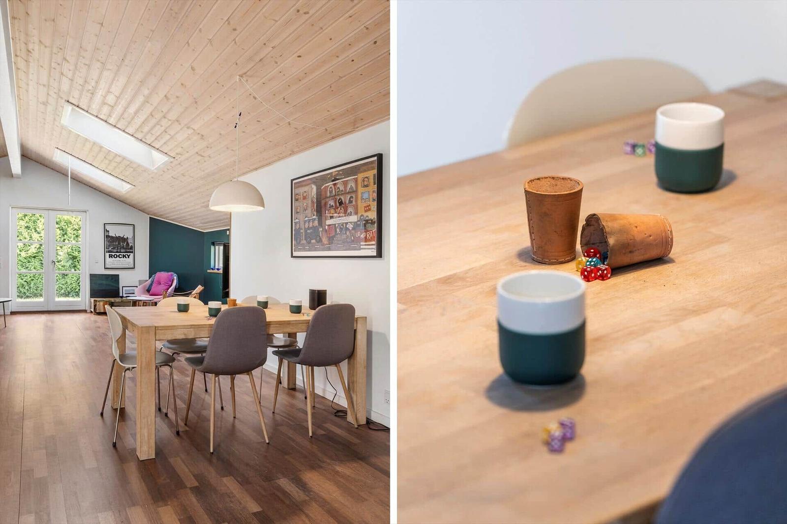 Essbereich mit Holztisch, Stühlen und Deckenfenstern. Tisch mit Tassen und Würfeln.
