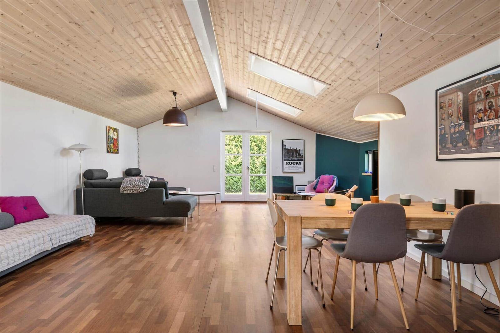 Wohn- und Essbereich mit Holzdecke, Tisch, Stühlen und Sofa.