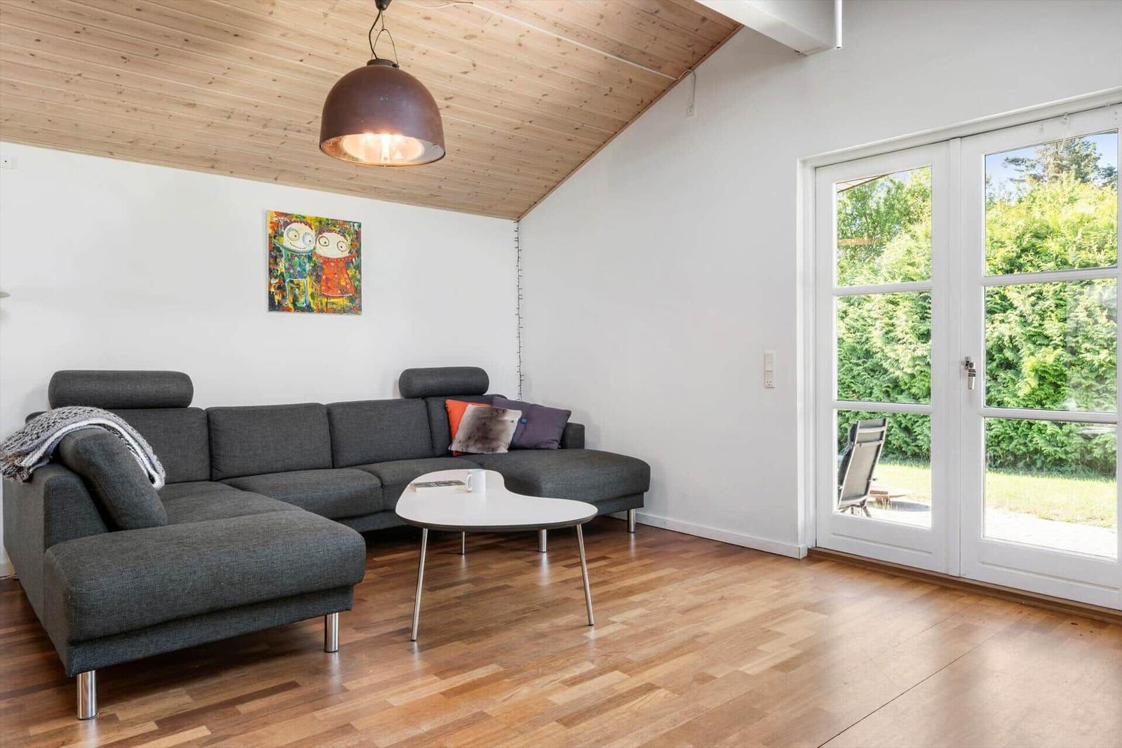 Wohnzimmer mit grauem Sofa, Holzboden und Fenster zur Außenterrasse.