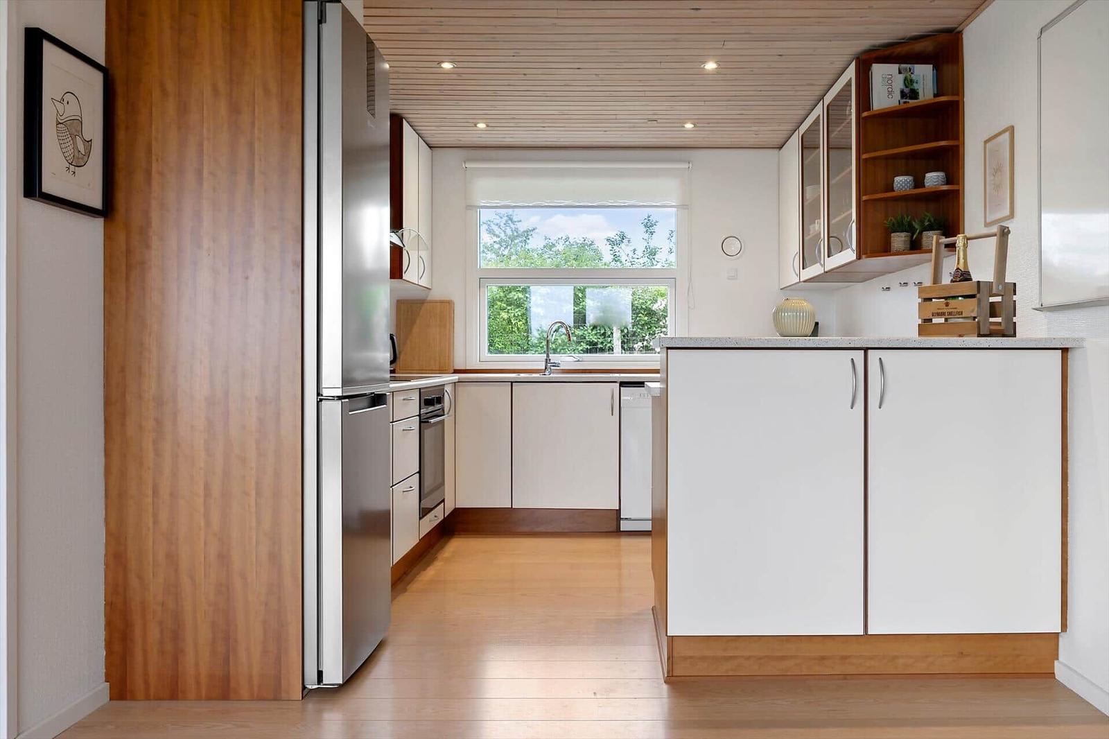 Modern kitchen with wooden floor, white cabinets, and stainless steel refrigerator.