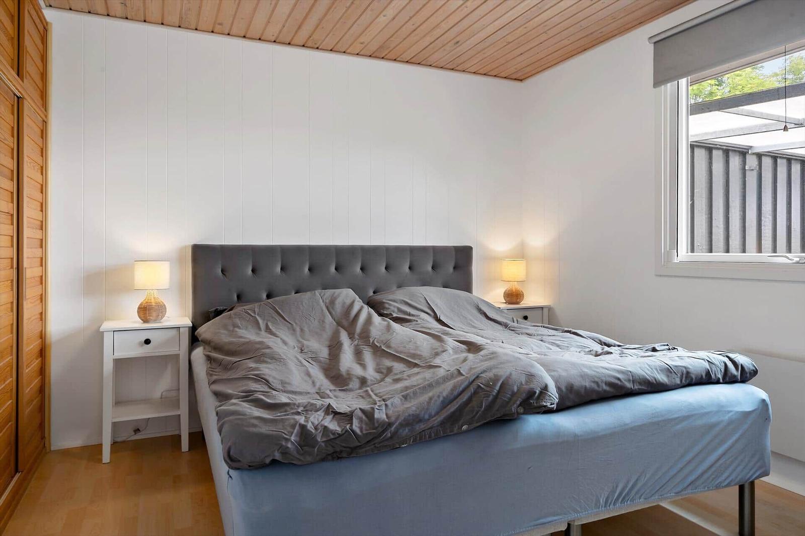 Bedroom with bed, nightstands, and window. Wooden ceiling and white walls.