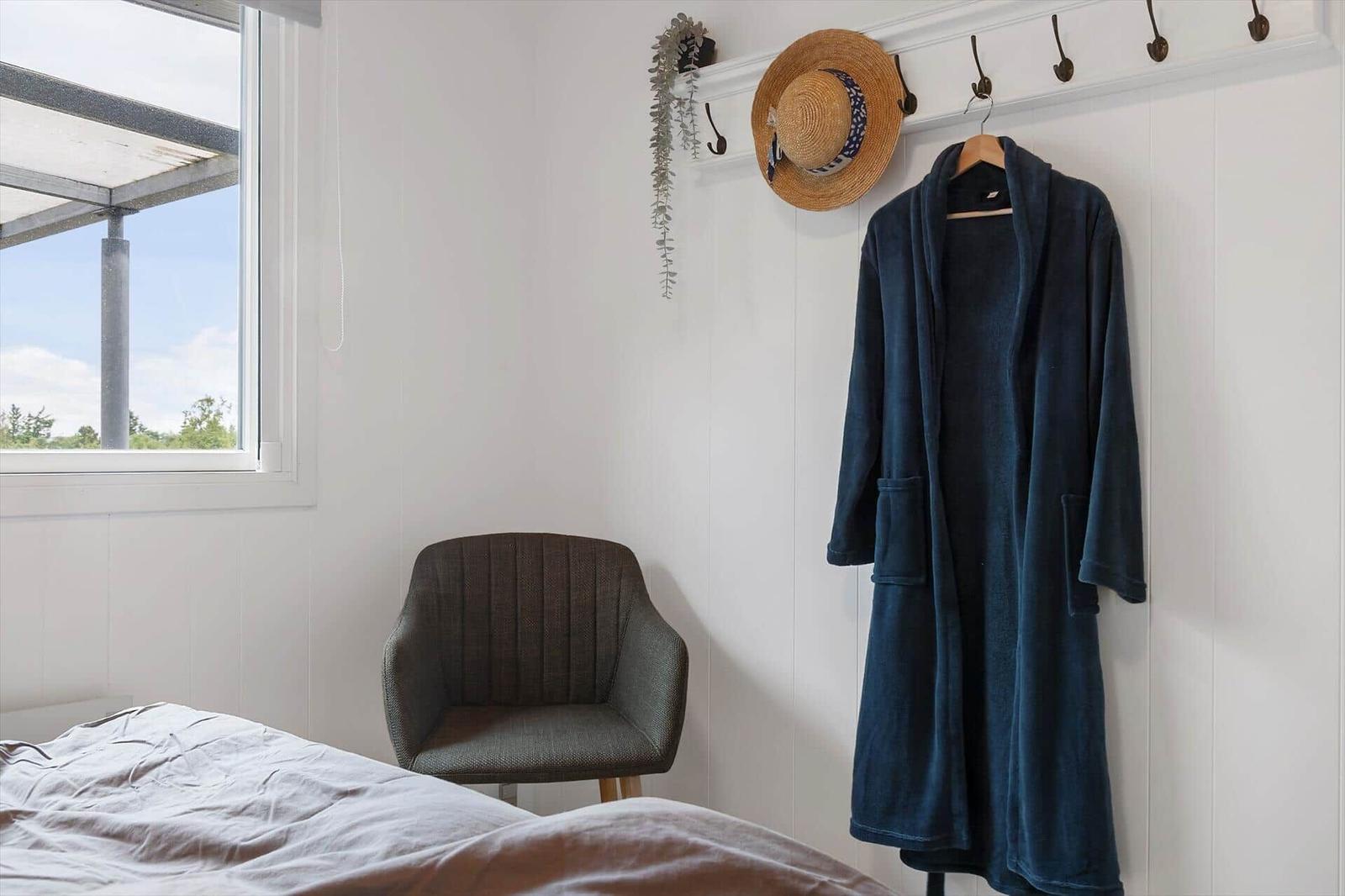 A bed, chair, and robe hang on a wall with hooks and a window.