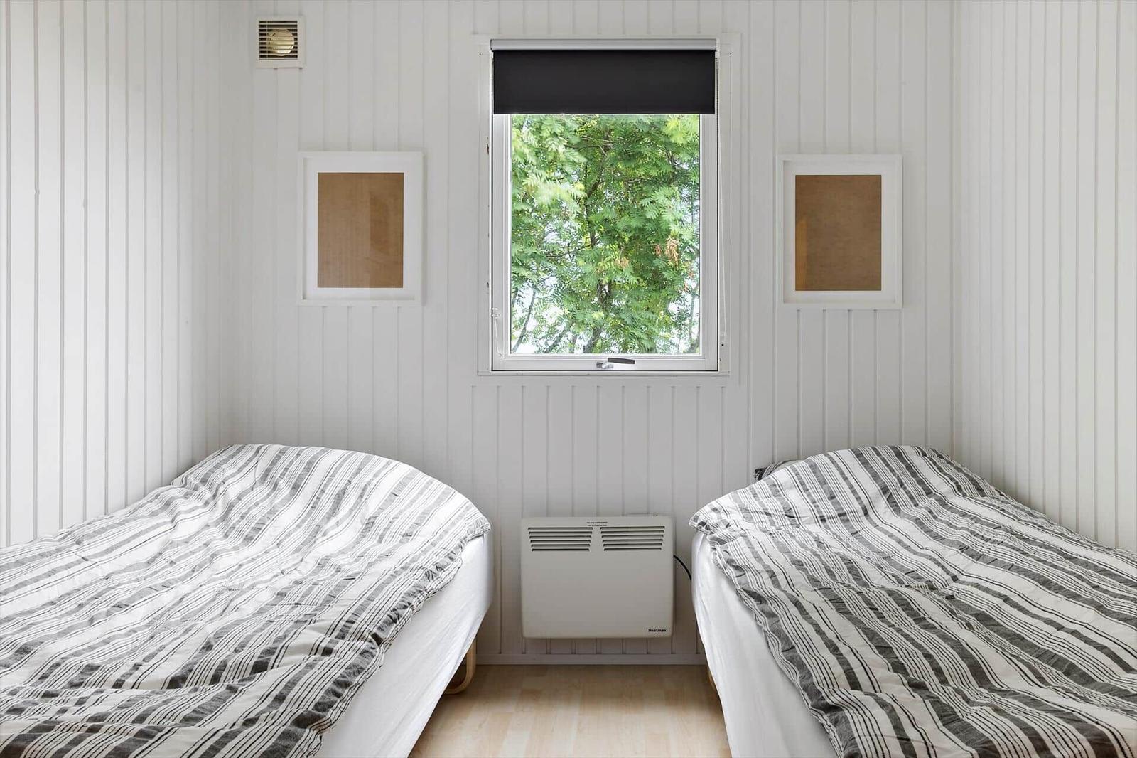 Two beds with striped bedding in a room with white paneling and window overlooking trees.