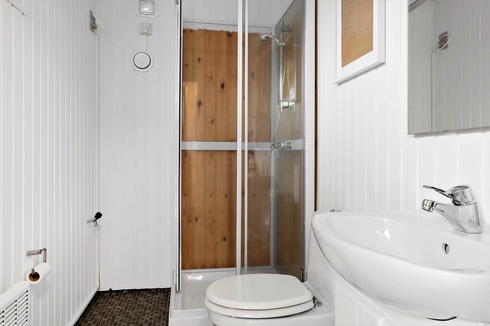 Bathroom with shower, toilet, and sink. Wooden wall in shower area.