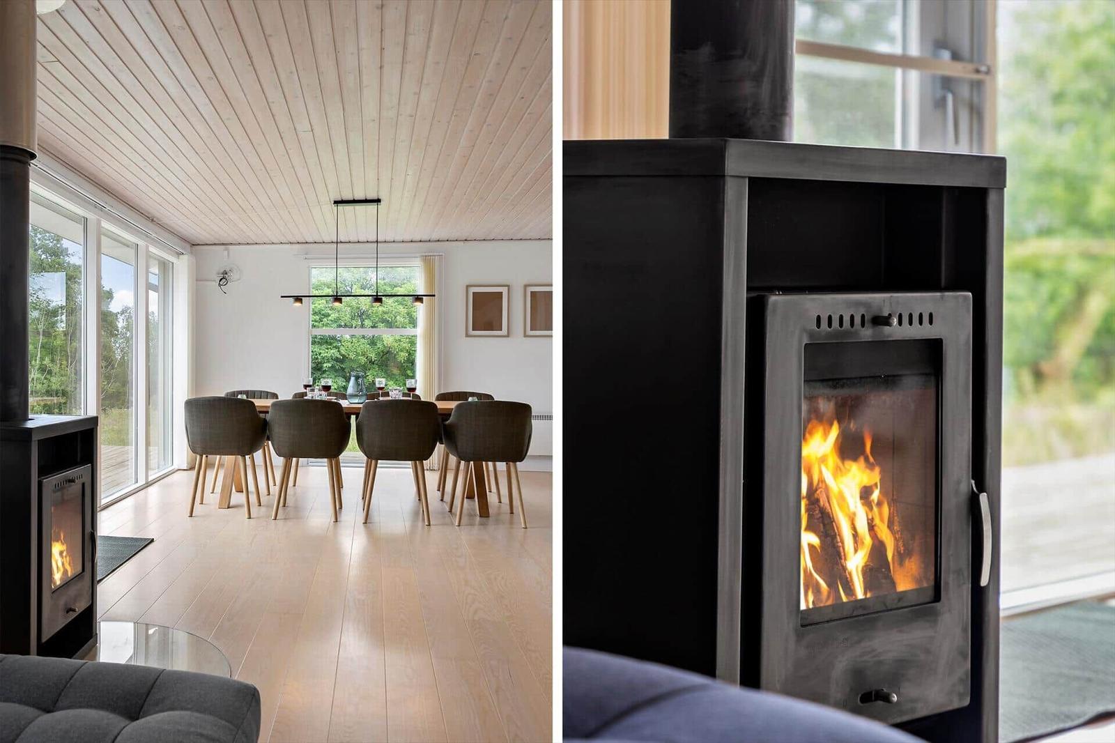 Modern living and dining area with wood-burning stove. Wooden ceiling and large windows.