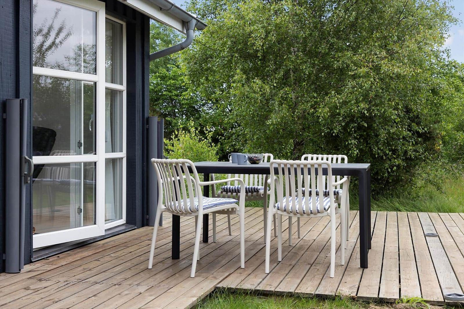 Deck with table and chairs in front of a house with glass doors.