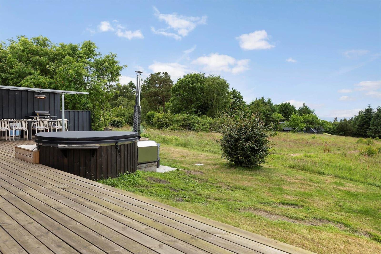 High-quality hot tub on wooden terrace with grill and seating area in the green.
