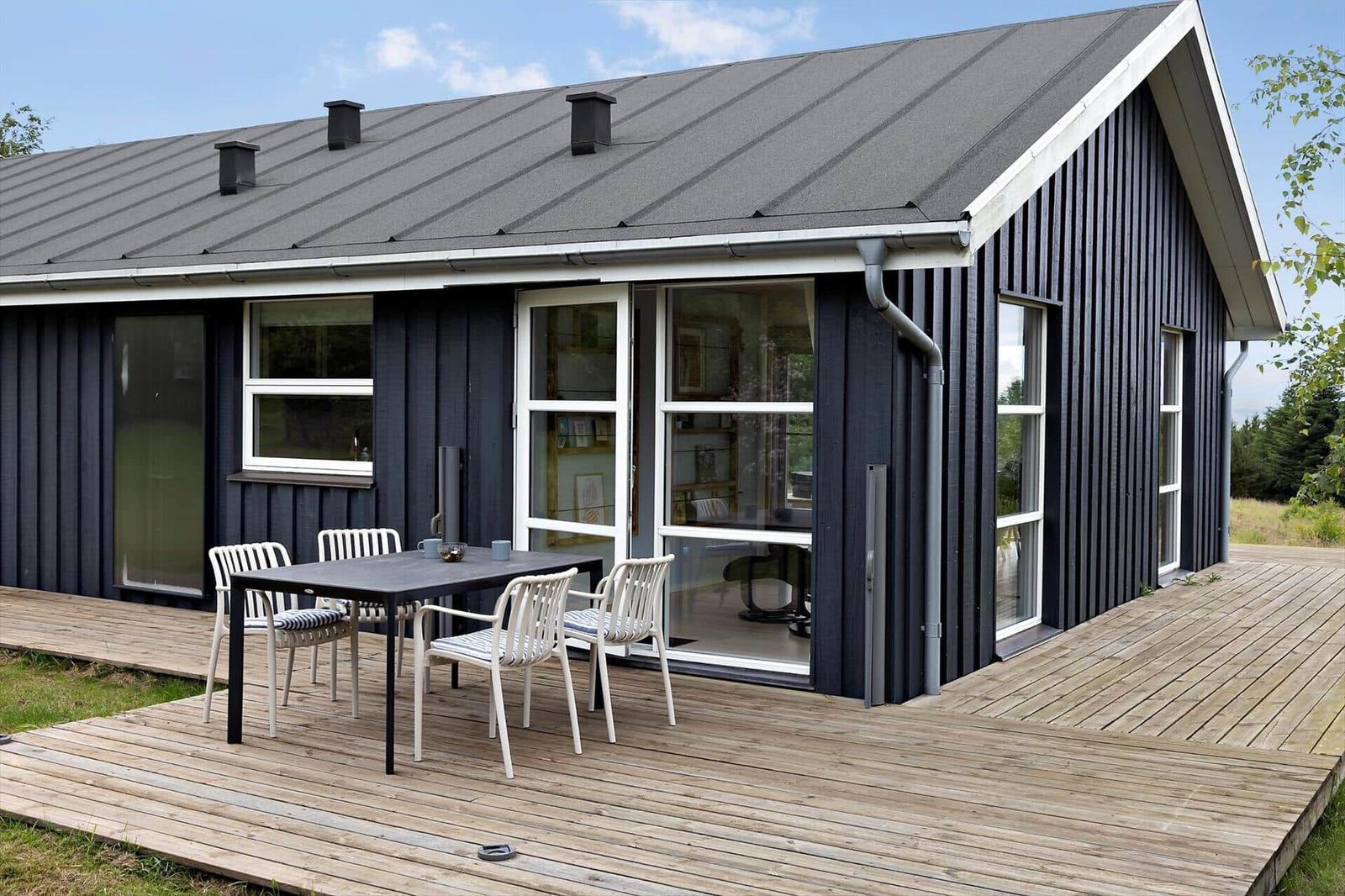 Modern wooden cabin with terrace and seating area. Large windows and roof vents.