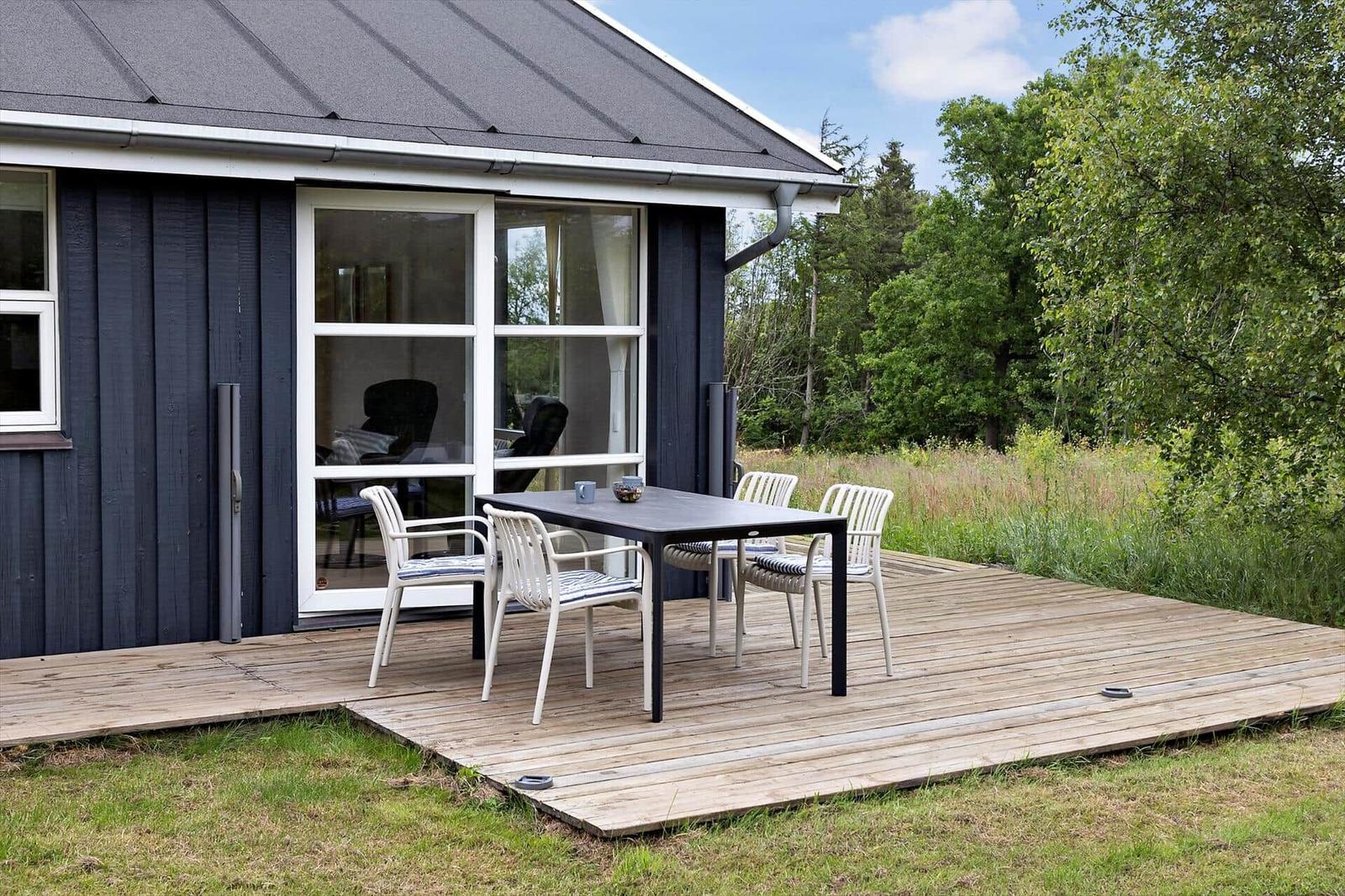Deck with table and chairs in front of a house with dark wood and glass windows.