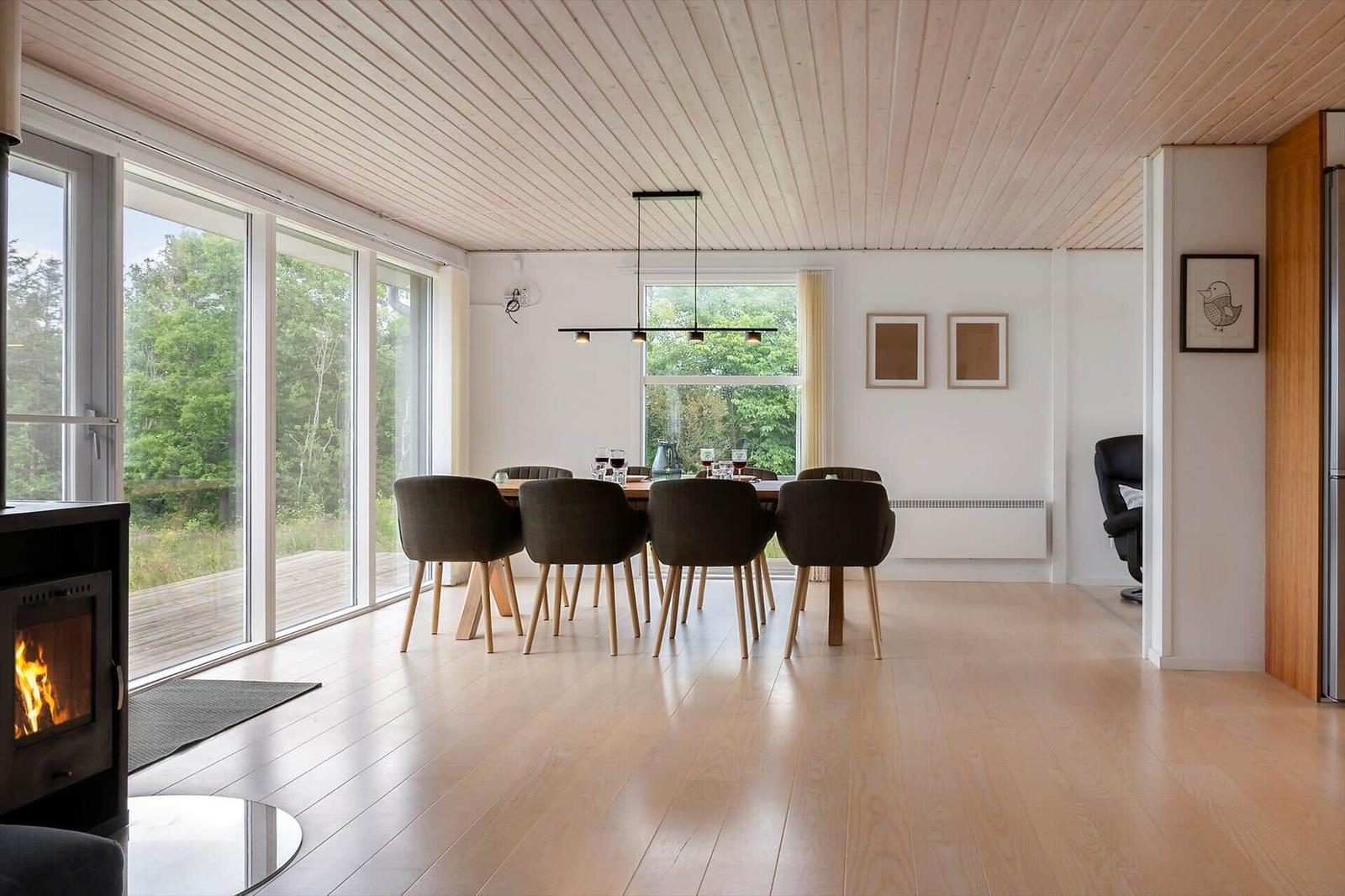 Dining area with wooden floor, large windows, and dining table with chairs. Fireplace in foreground.