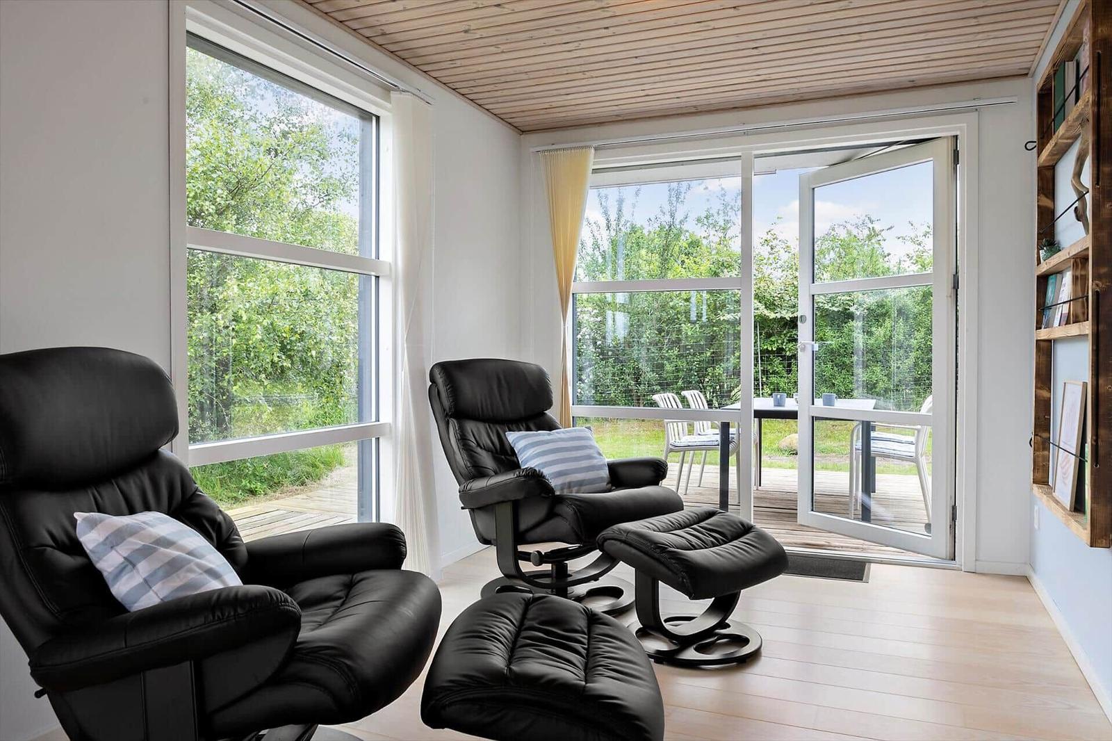 Two black recliners with cushions are by large windows. Through the glass door, a terrace with garden is visible.