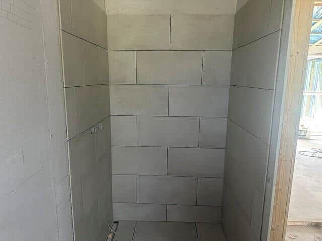 Dusche mit grauen Fliesen und offener Tür zur Baustelle.