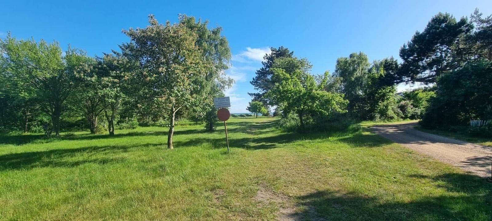 Grünes Feld mit Bäumen und einem Weg. Ein Schild steht im Vordergrund.