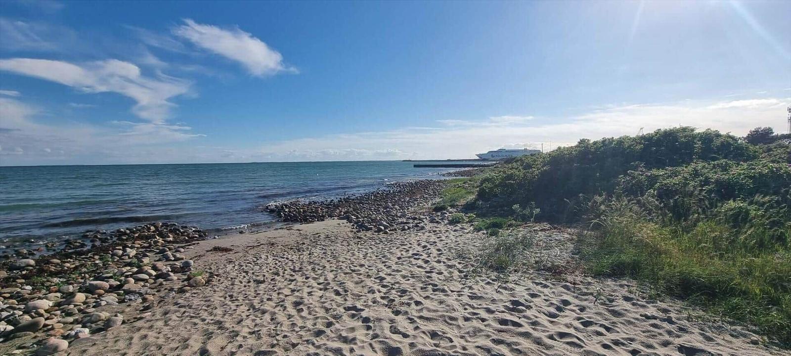 Strand mit Sand und Steinen, Blick auf das Meer und ein Schiff im Hintergrund.