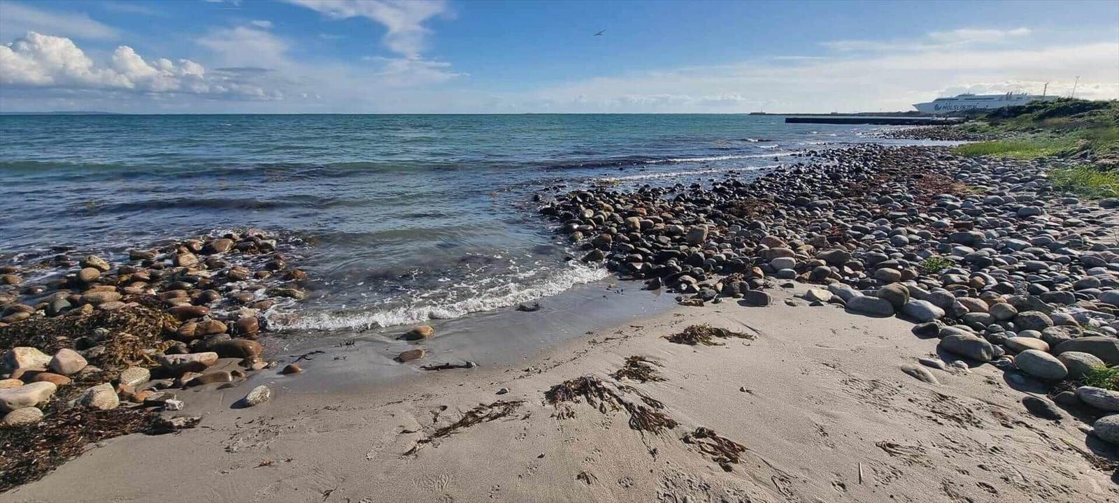 Strand mit Steinen und Sand, Meer und Himmel im Hintergrund.