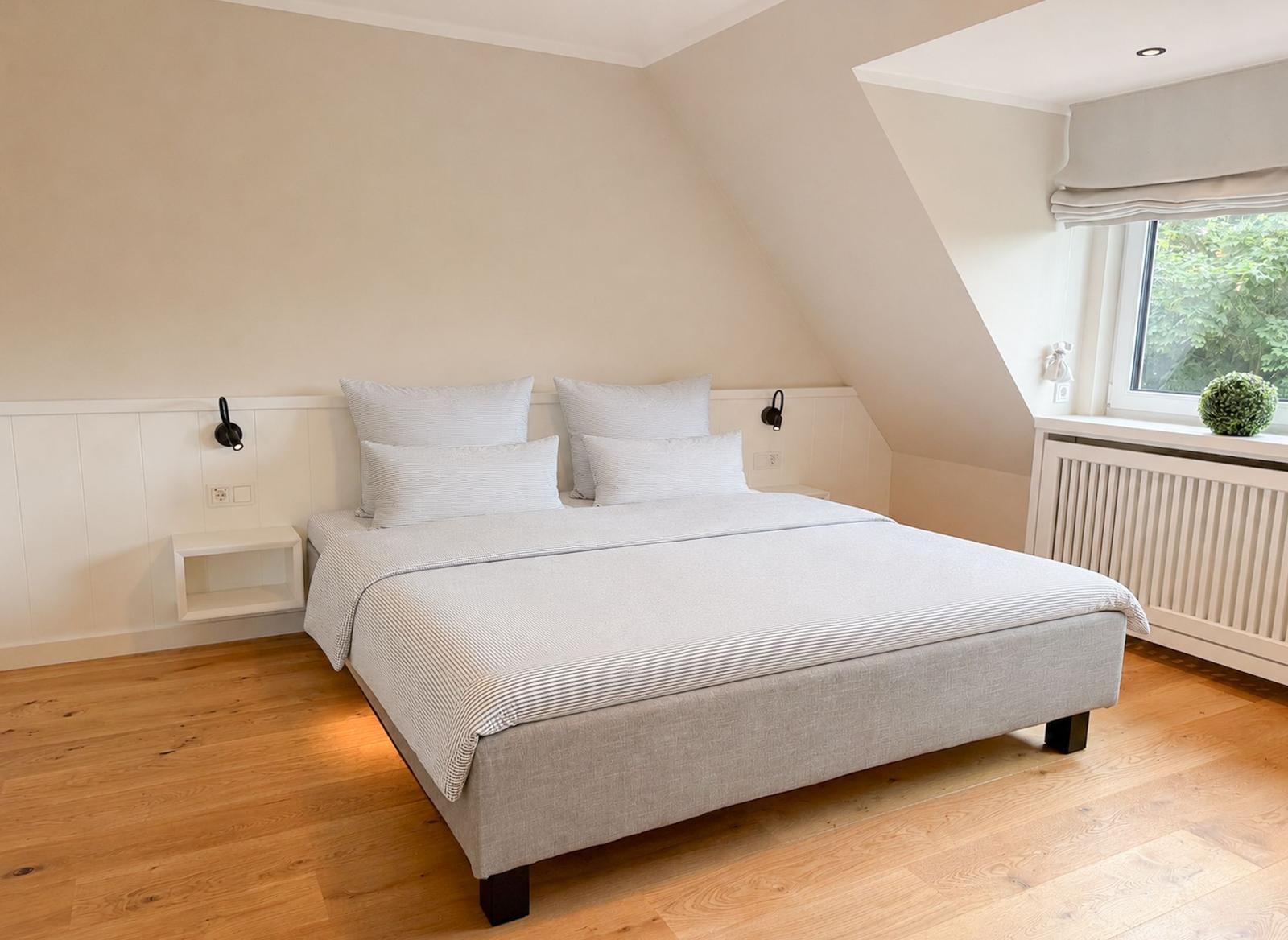 Schlafzimmer mit Doppelbett, Holzboden und Fenster mit Blick auf Grün.