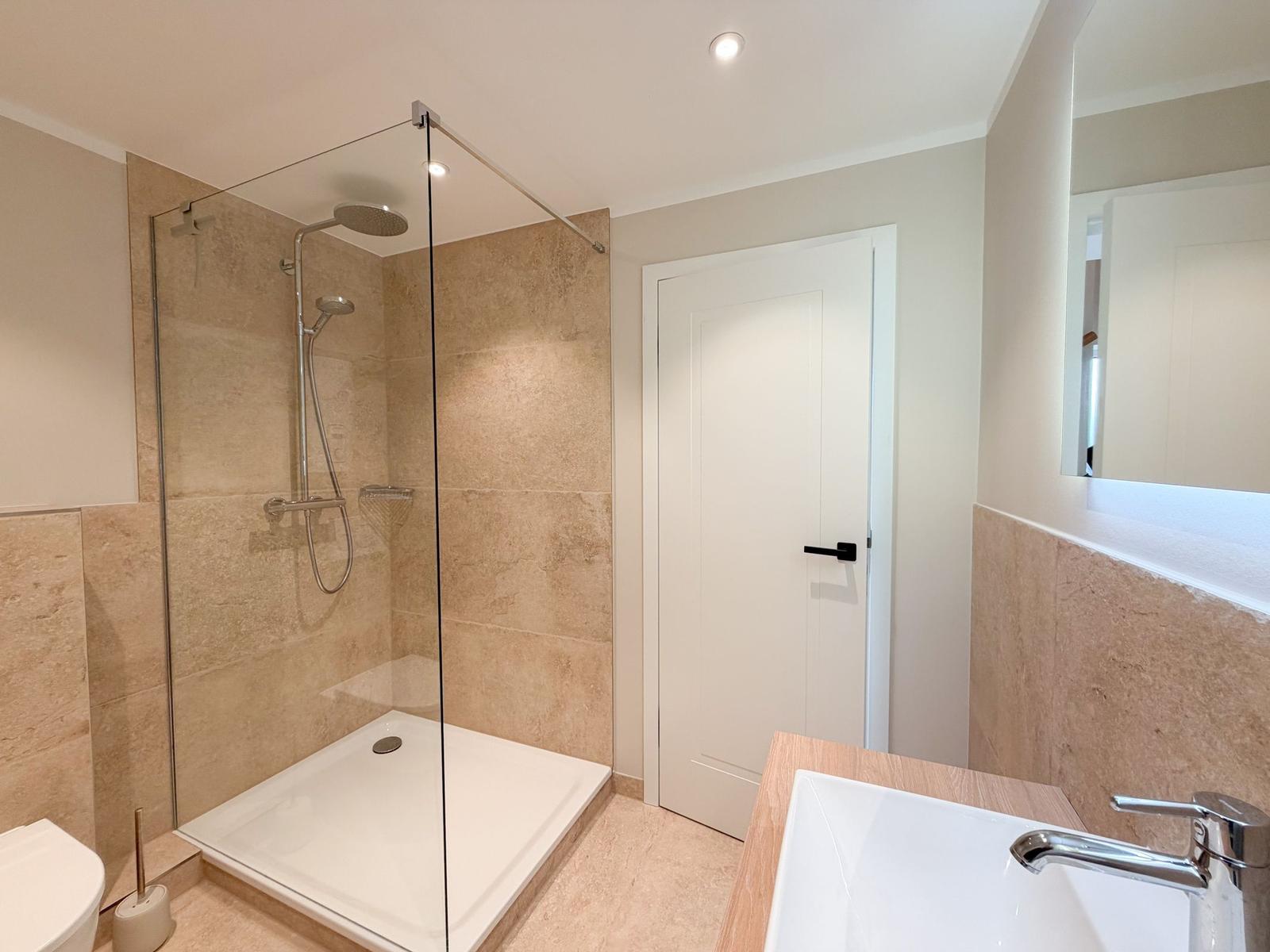 Badezimmer mit Dusche, Waschbecken und Toilette. Wandfliesen und Spiegel.