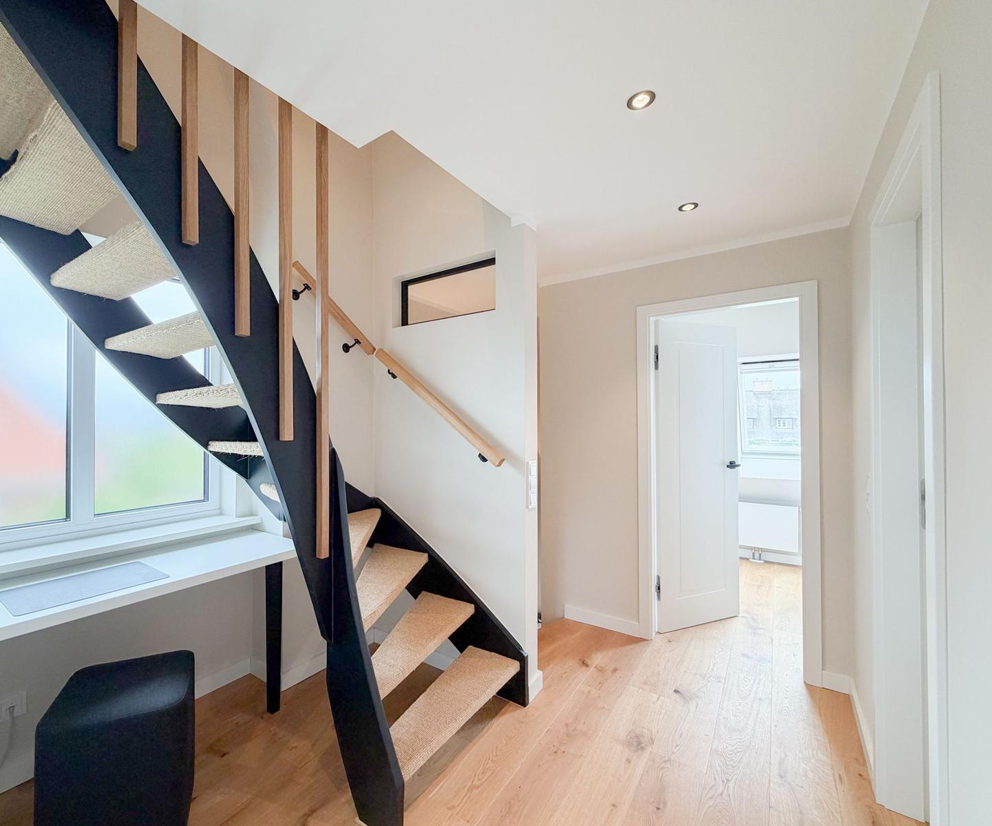Treppe mit Holzgeländer und Sitzbank neben Fenster. Holzboden und helle Wände.