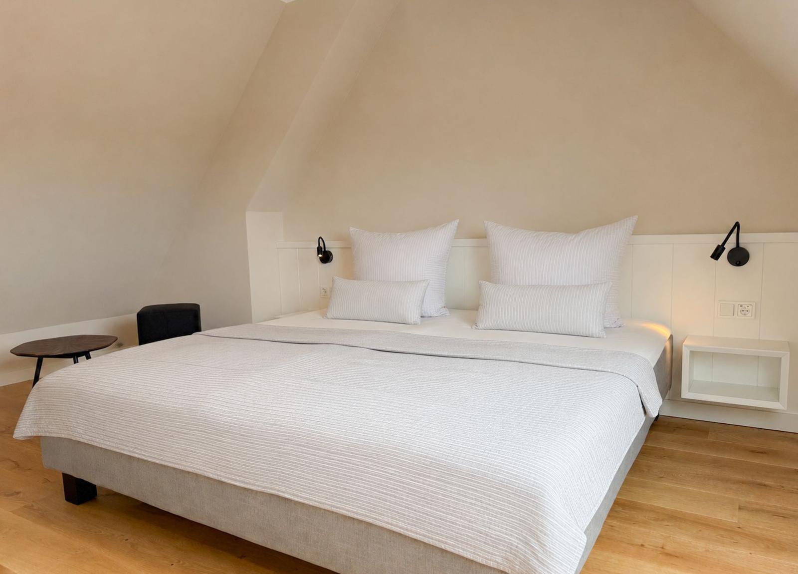 Schlafzimmer mit Doppelbett, weißen Kissen und Holzboden unter schrägen Wänden.