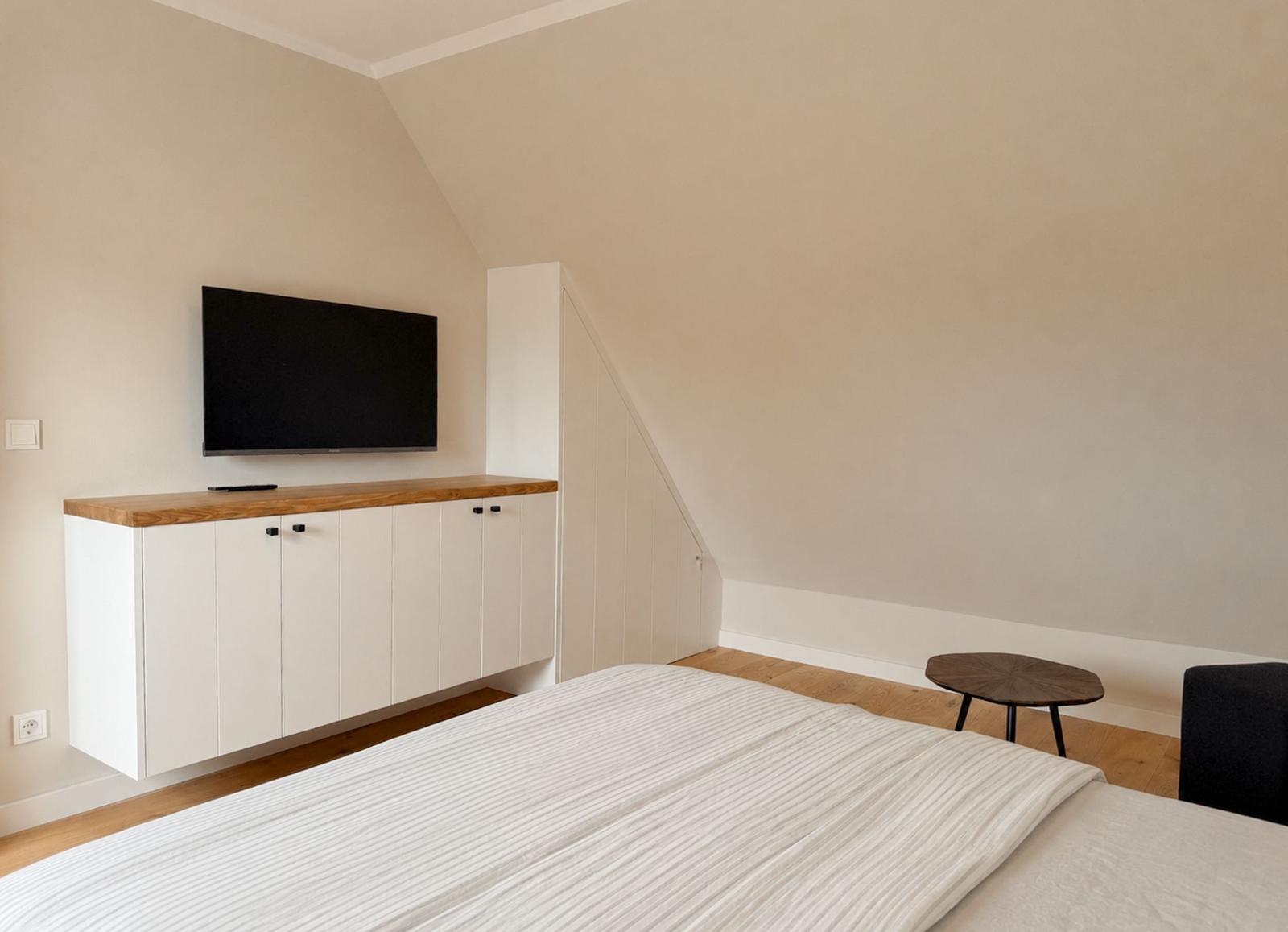 Schlafzimmer mit Bett, TV und Holzregal an der Wand