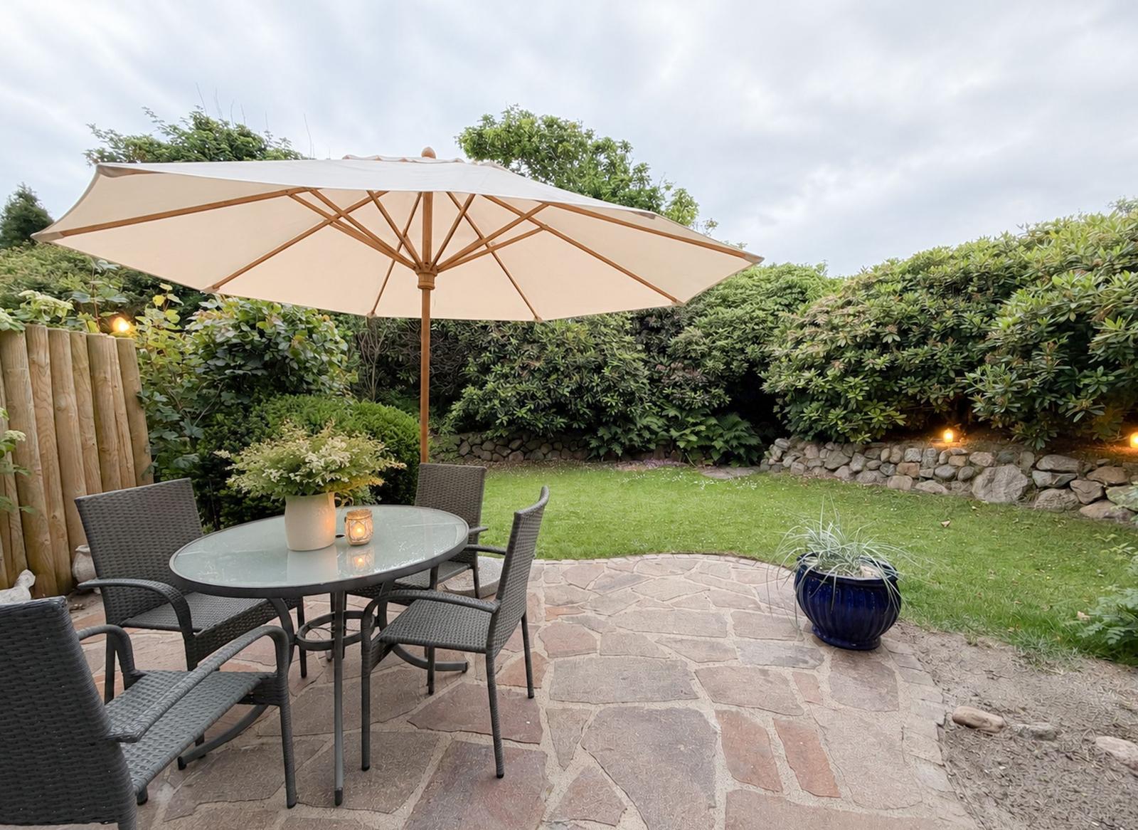 Garten mit Tisch, Stühlen und Sonnenschirm auf Steinplatten.