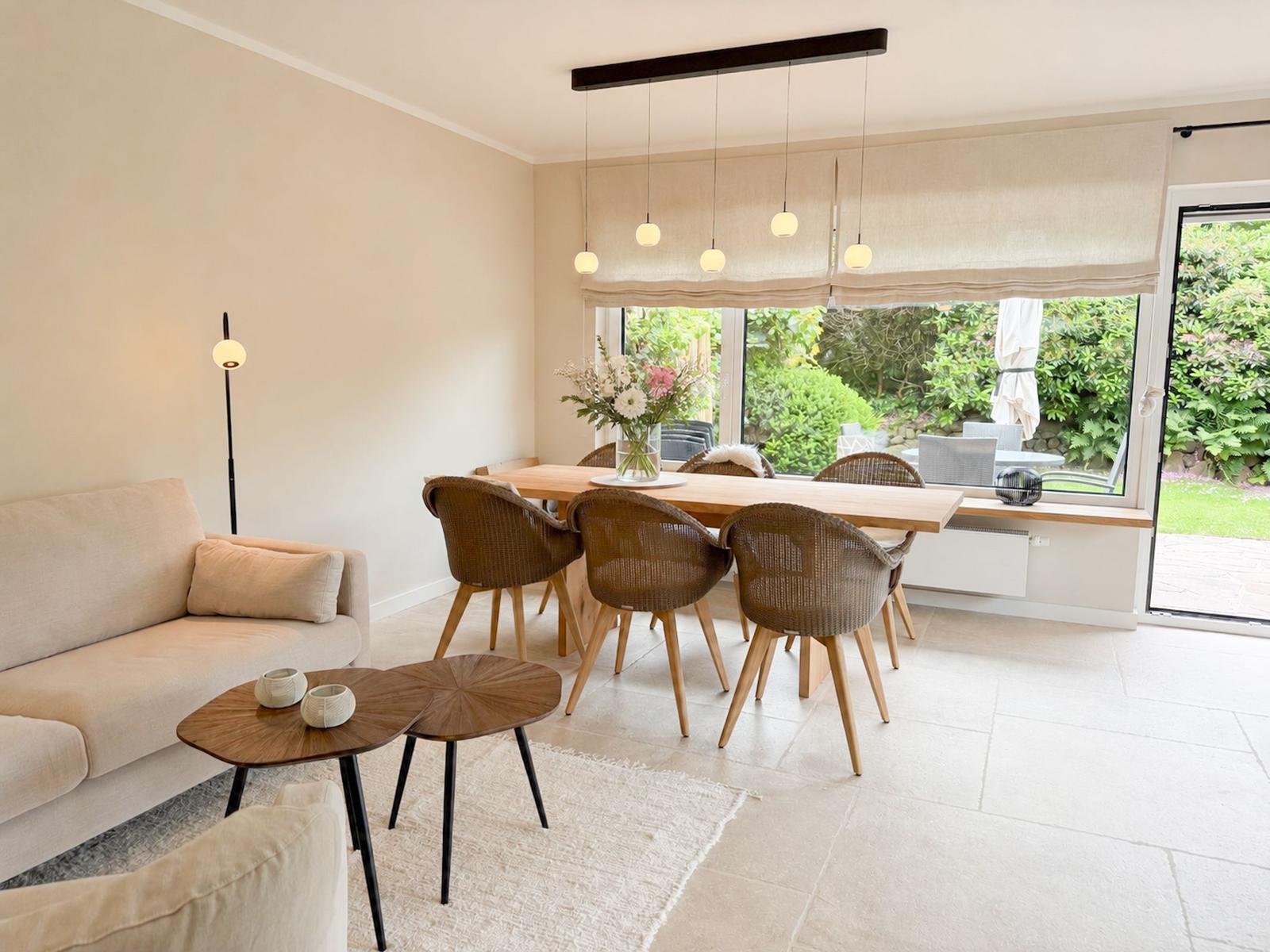 Wohn- und Essbereich mit Sofa, Tisch und Stühlen. Fenster zur Terrasse mit Gartenblick.