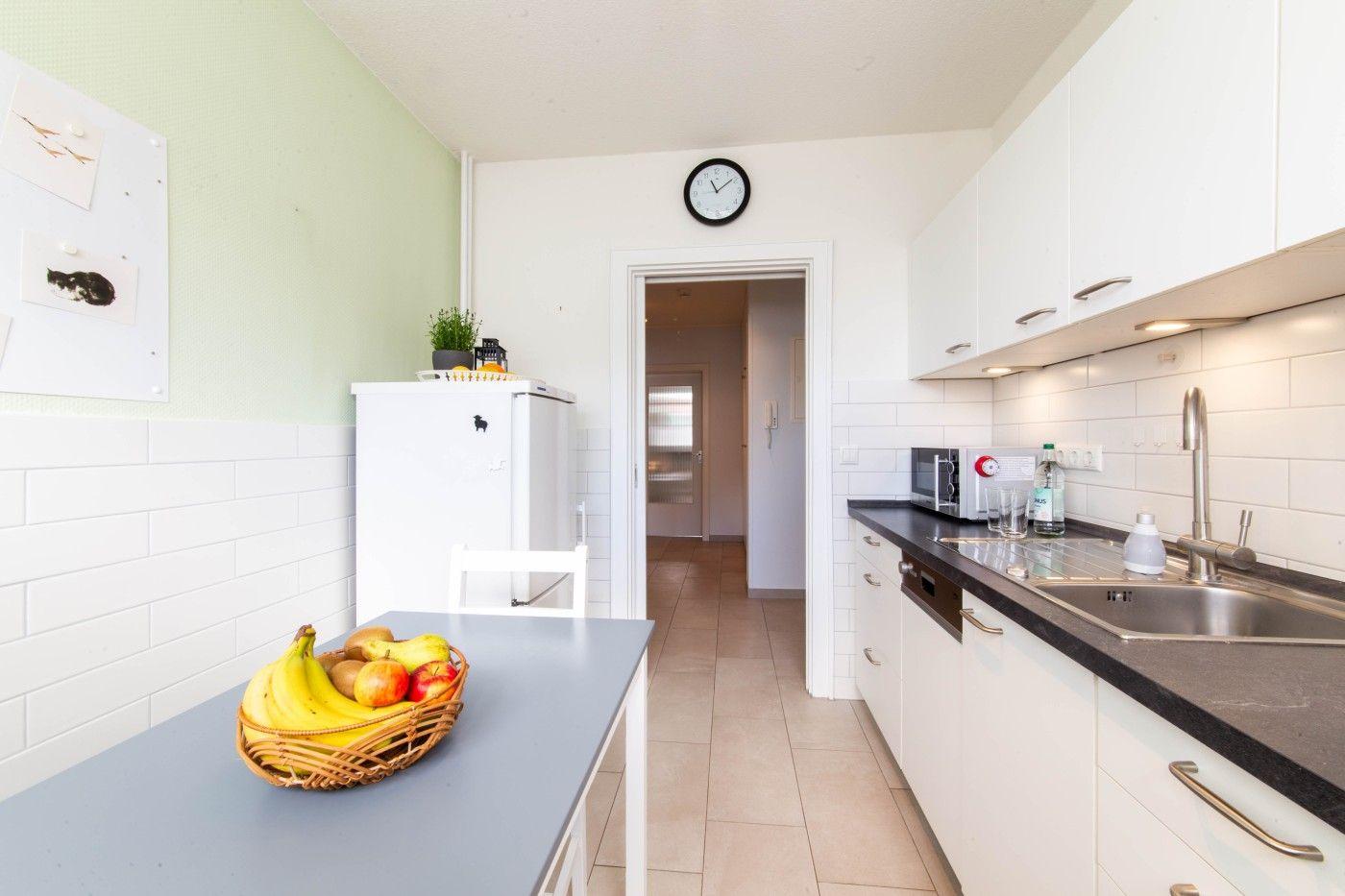 Küche mit Arbeitsplatte, Spüle, Kühlschrank und Obst auf Tisch.