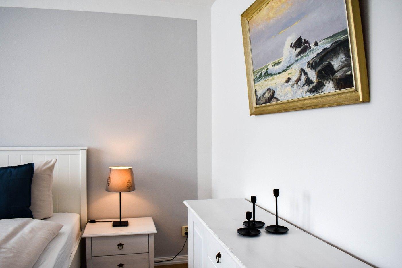 Schlafzimmer mit Bett, Nachttisch, Schrank und Wandbild mit Meeresmotiv.
