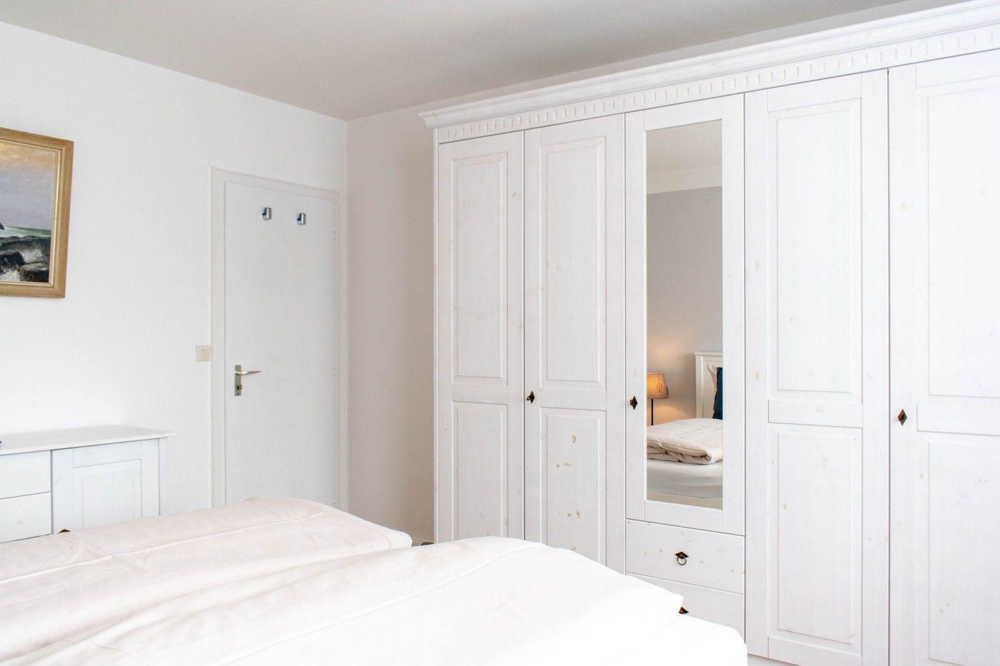 Schlafzimmer mit weißem Schrank und Bett. An der Wand hängt ein Bild.