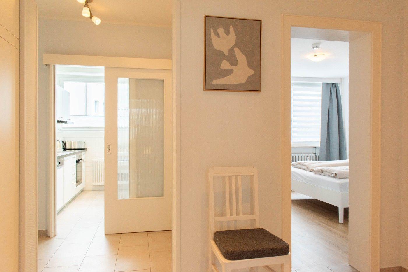 Haus mit Küche, Schlafzimmer und Stuhl im Flur. Wandbild mit zwei Vögeln.
